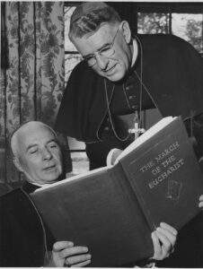 Bishop Walsh leans over another bishop's shoulder.
