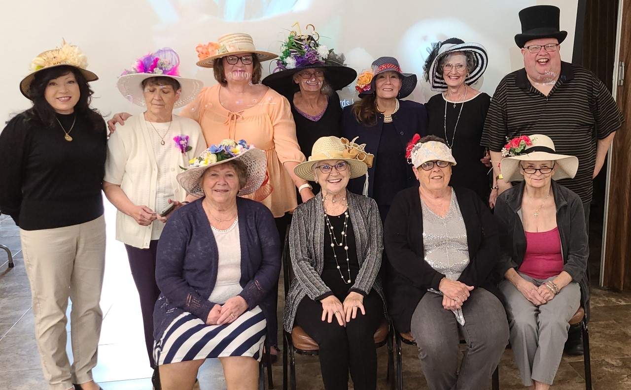 Ten women and Fr. Misbrenner pose with hats on at the Kentucky Derby party.