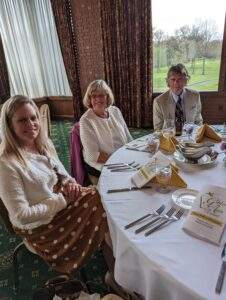 Three attendees smile at the camera, seated at their dinner tables.