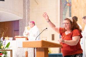 Woman stands at ambo with raised hand