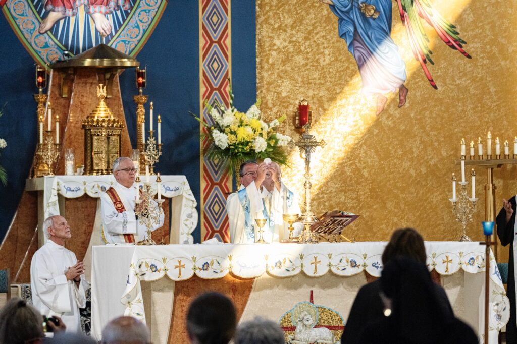 Bishop Bonnar raises the eucharist, illuminated by sun coming through the window for the Assumption Pilgrimage in North Jackson. Photo by Brian Keith.