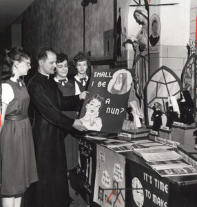 Father Francis Snock assistant pastor of then St. Matthias Parish views vocation posters offered by the 9th Graders of the parishes Junior High School.